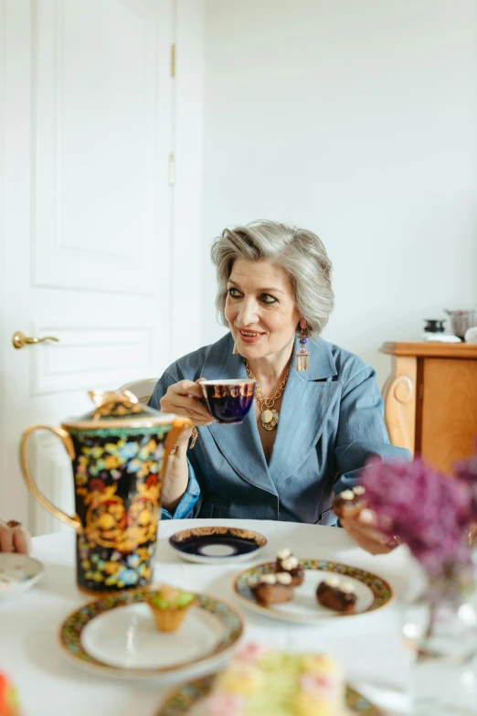 a couple of people that are sitting at a table, a colorized photo, by Anna Haifisch, trending on pexels, wearing silver silk robe, woman drinking coffee, grandma, confident looking