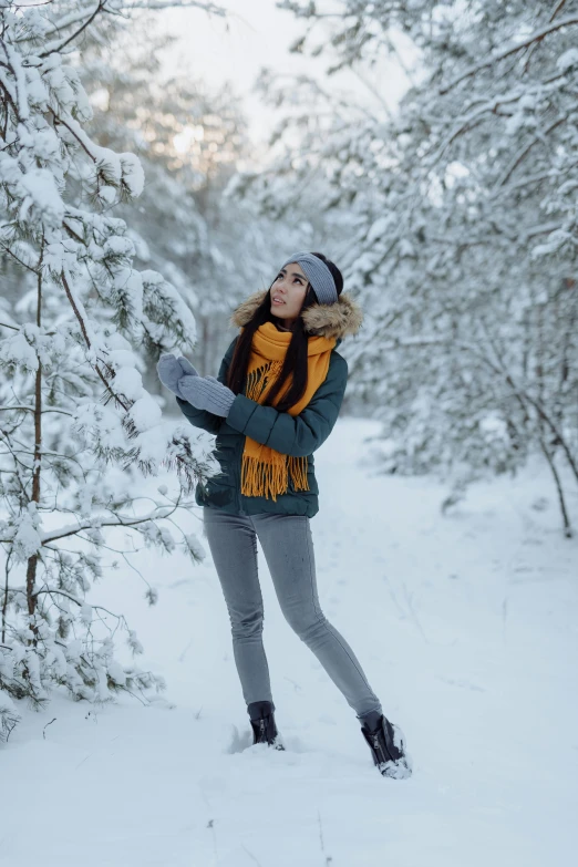 a woman standing in the middle of a snow covered forest, doing a sassy pose, gray and orange colours, holiday, 2019 trending photo
