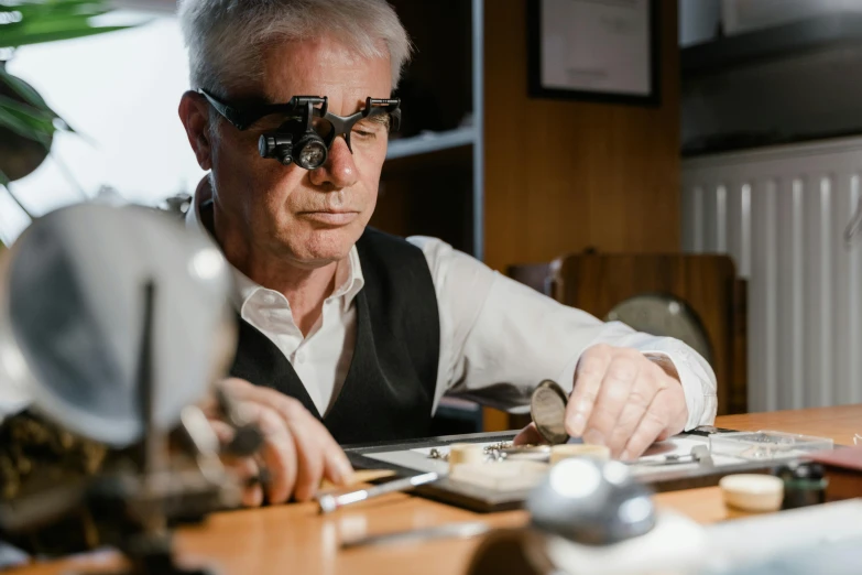 a man sitting at a table with a pair of glasses on his face, by Lee Loughridge, pexels contest winner, renaissance, professional gunsmithing, platinum jewellery, thumbnail, plating