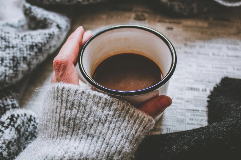 a person holding a cup of coffee in their hands, a photo, by Lucia Peka, trending on pexels, brown sweater, vintage photo, thumbnail, cold