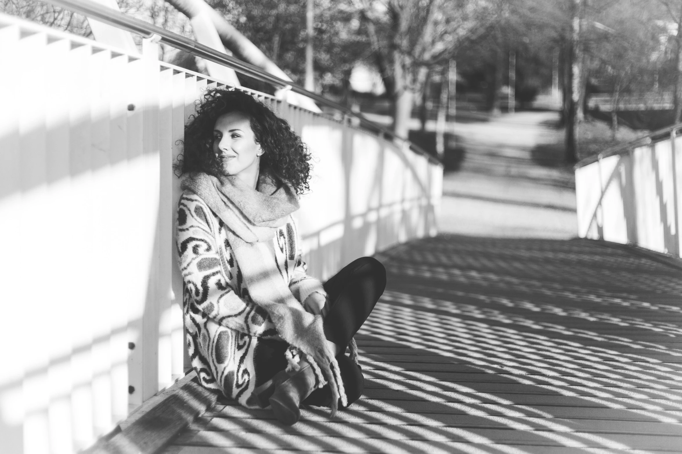 a black and white photo of a woman sitting on a bridge, a black and white photo, curly haired, winter sun, sitting on the floor, street photo