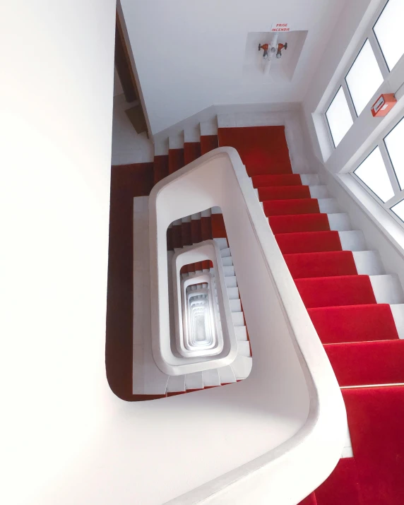 a spiral staircase in a building with red carpet, inspired by Ricardo Bofill, unsplash contest winner, bauhaus, white red, lgbtq, dezeen showroom, high - angle view