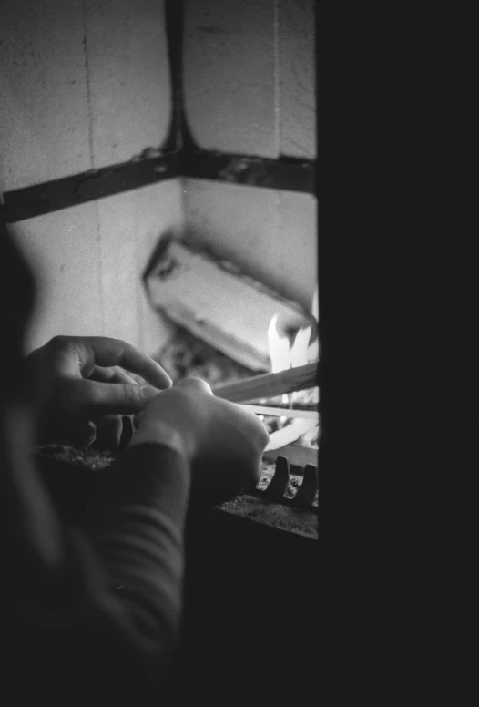 a black and white photo of a person in a kitchen, inspired by Sergio Larraín, process art, burning hands, cosy fireplace, crafting, evening time