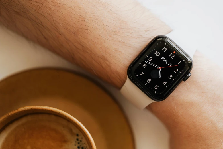 an apple watch sitting on a table next to a cup of coffee, trending on pexels, square, background image, arms crossed on chest, taken with sony alpha 9