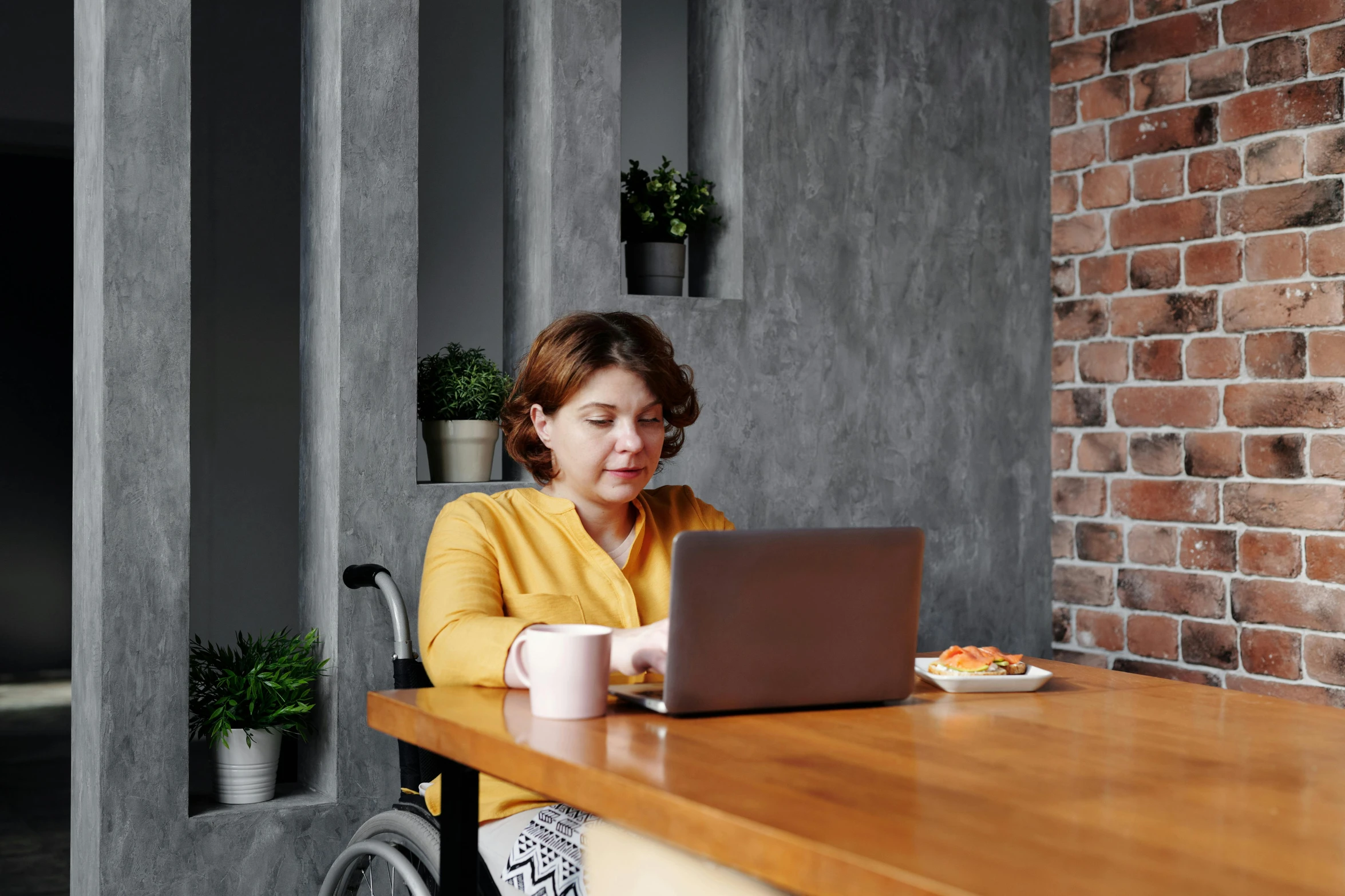 a woman sitting at a table with a laptop, sitting in a wheelchair, profile image