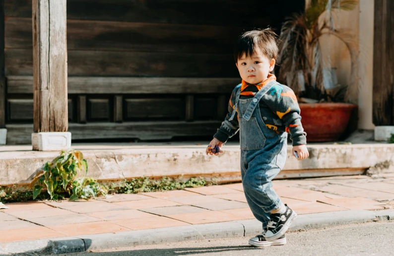 a young boy riding a skateboard down a street, pexels contest winner, happening, overalls, 2 years old, standing outside a house, asian male