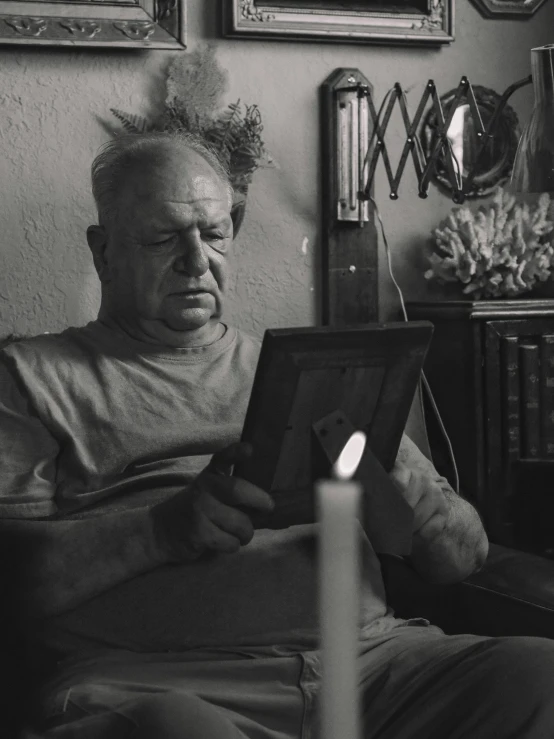 a man sitting in a chair reading a book, a black and white photo, on a candle holder, stanisław szukalski, looking sad, taken on a 2000s camera