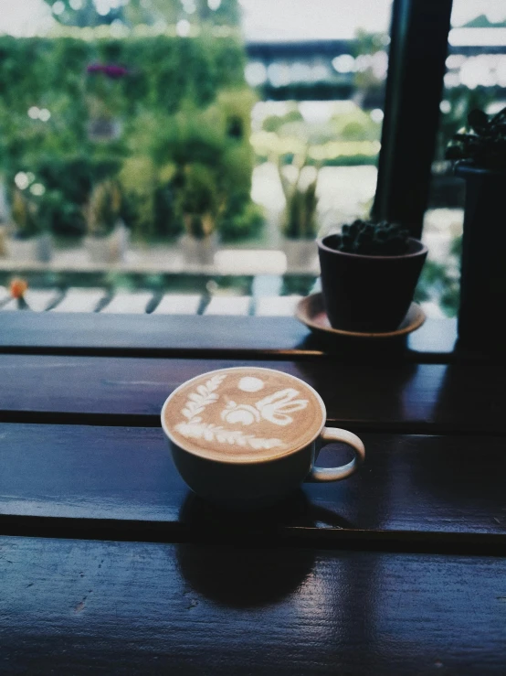 a cup of coffee sitting on top of a wooden table, by Yosa Buson, low quality photo, ((oversaturated)), window, latte art