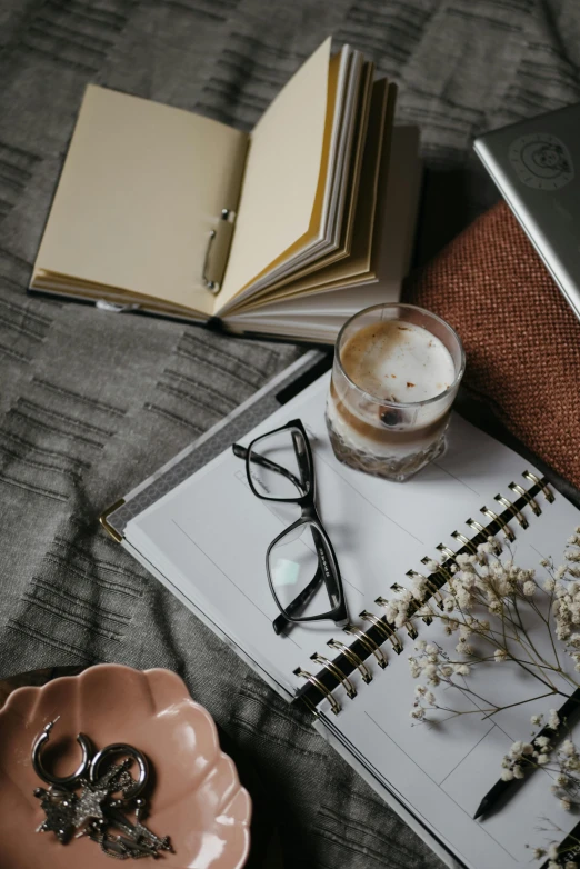 an open notebook sitting on top of a bed next to a cup of coffee, a still life, trending on unsplash, square rimmed glasses, high quality photo, looking seductive, sitting on a mocha-colored table