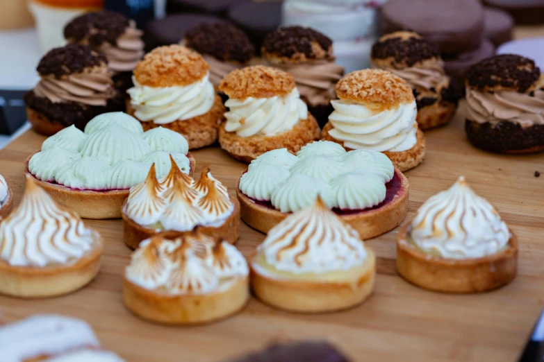 a table topped with lots of cupcakes covered in frosting, by Lee Loughridge, trending on unsplash, on a wooden plate, pastries, in a row, thumbnail