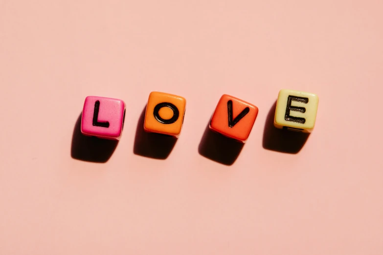 the word love spelled with wooden letters on a pink background, by Olivia Peguero, trending on pexels, pop art, squares, orange pastel colors, beads, pink and black