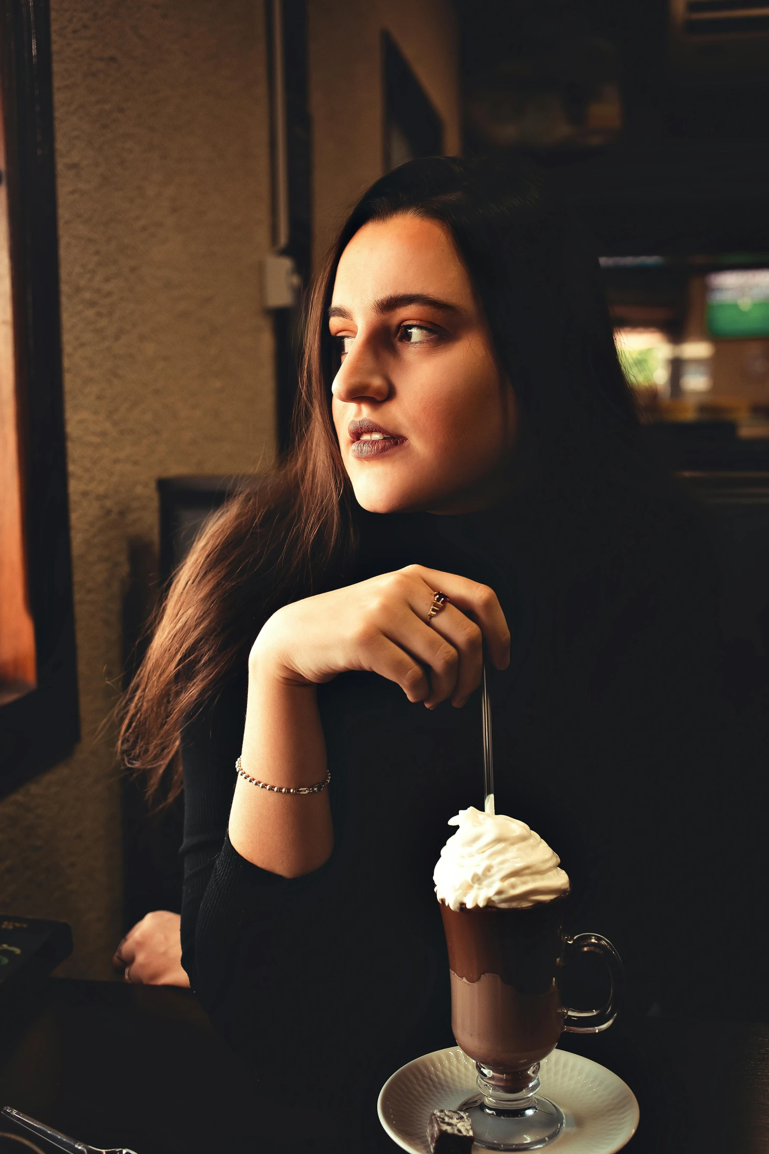 a woman sitting at a table with a cup of coffee, a picture, inspired by Elsa Bleda, pexels contest winner, renaissance, young middle eastern woman, ice cream on the side, in a black hoodie, low quality photo