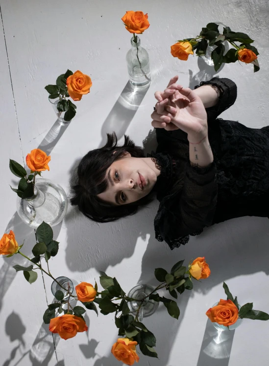 a woman laying on a floor surrounded by flowers, an album cover, by Winona Nelson, pexels contest winner, finn wolfhard, laying on roses, gothic aesthetic, on a white table