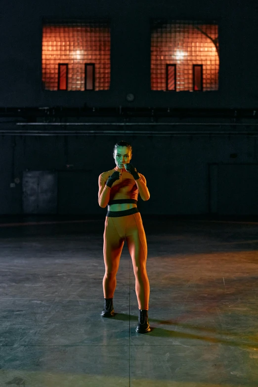 a woman standing in a dark room holding a tennis racquet, inspired by Vanessa Beecroft, holography, in a boxing ring, orange and yellow costume, kickboxing, official music video