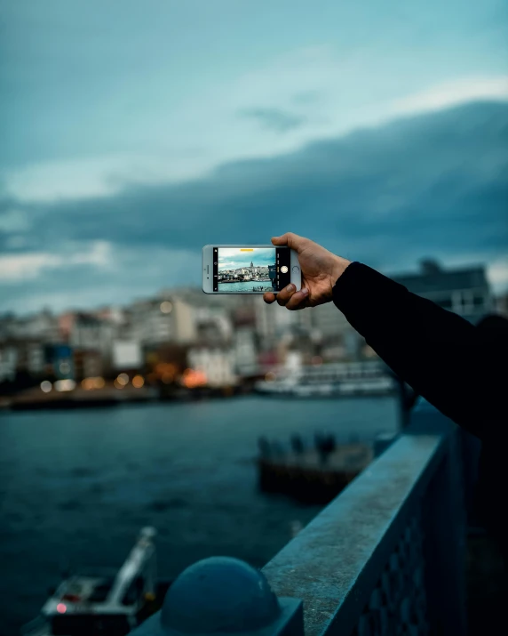 a person taking a picture of a body of water, in a city, in the evening, lgbtq, phone in hand