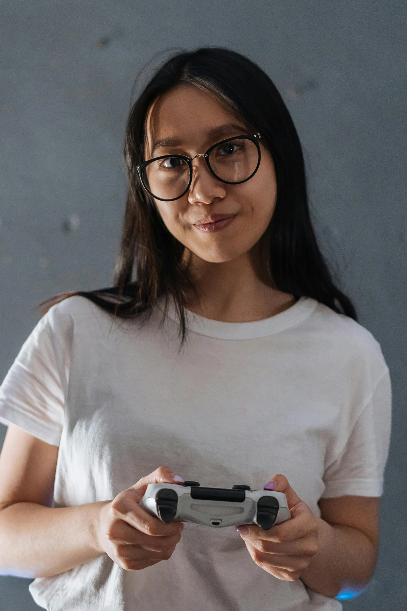 a woman holding a video game controller in her hands, inspired by Feng Zhu, pexels contest winner, realism, wearing a light shirt, wearing small round glasses, on a gray background, asian descent