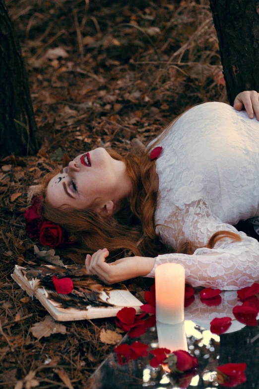 a woman laying on the ground next to a candle, an album cover, pexels contest winner, romanticism, ritual in a forest, white and red roses, grim fashion model looking up, corpse bride style