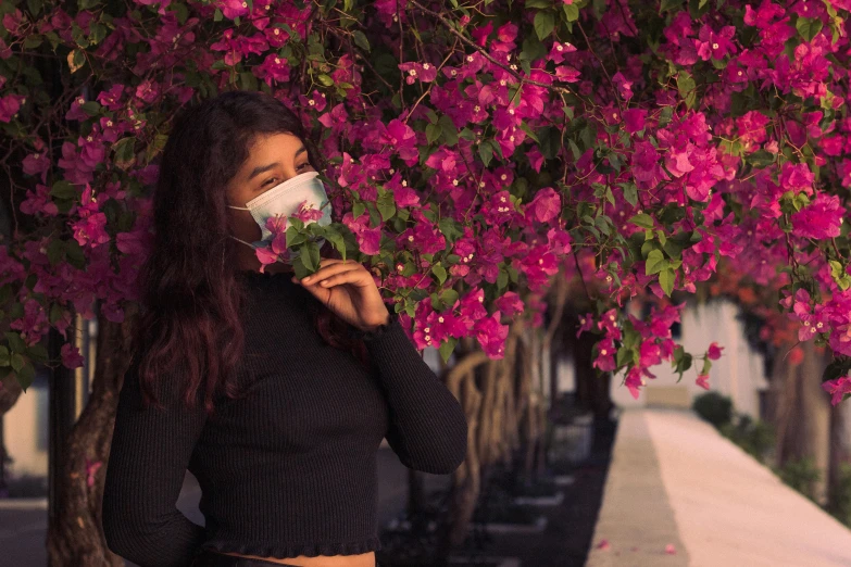 a woman wearing a face mask standing in front of a tree, pexels contest winner, bougainvillea, dua lipa, pollution, avatar image