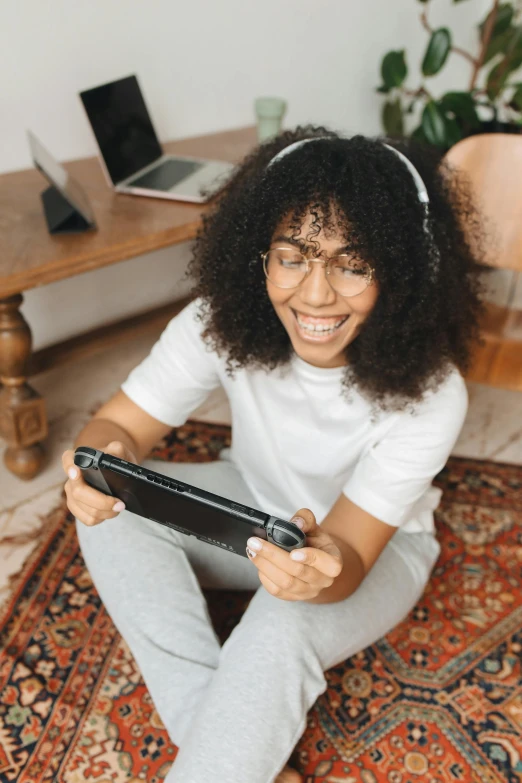 a woman sitting on the floor holding a nintendo wii controller, pexels contest winner, happening, afro tech, using a magical tablet, happily smiling at the camera, avatar image