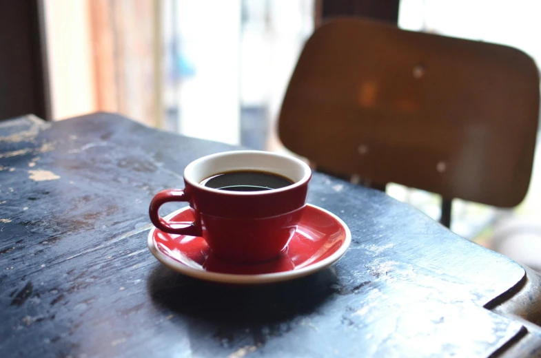 a cup of coffee sitting on top of a red saucer, unsplash, photorealism, medium format, cafe tables, dark skinned, black and red suit