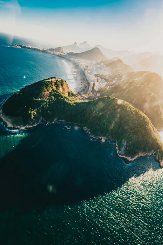 a small island in the middle of a body of water, a tilt shift photo, unsplash contest winner, rio de janeiro, sun flares, hills and ocean, flying islands