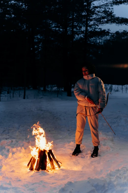 a man standing next to a fire in the snow, inspired by Einar Hakonarson, land art, ski mask, at twilight, white russian clothes, production photo