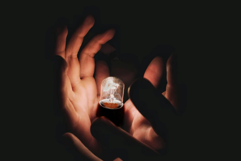 a person holding a light bulb in their hands, by Adam Marczyński, pexels contest winner, photorealism, lightning in a bottle, ferrofluid, vantablack chiaroscuro, small in size