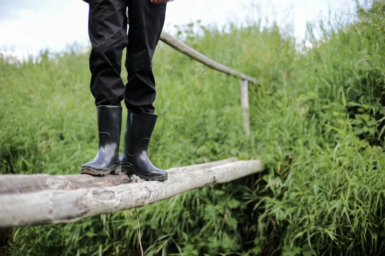 a person wearing rain boots standing on a log, black, wooden bridge, profile image, permaculture