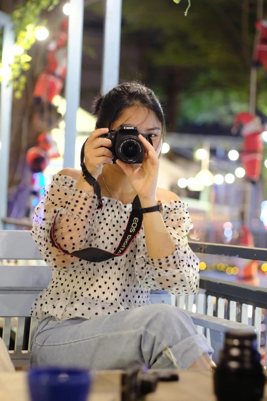 a woman sitting at a table taking a picture with a camera, dang my linh, polka dot, during night, profile image