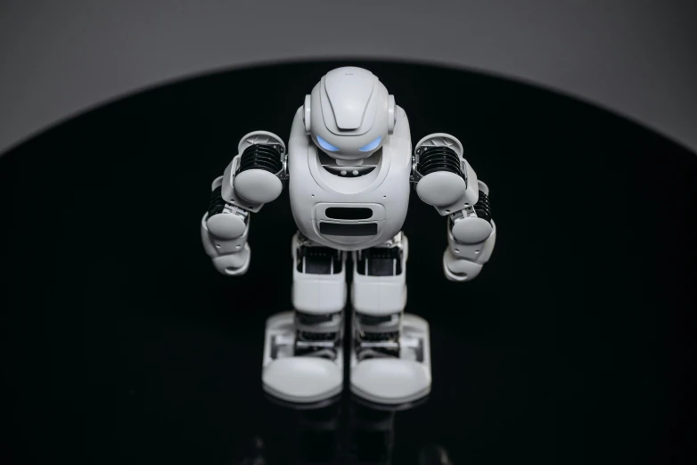 a close up of a toy robot on a table, standing with a black background, on a white table, cybertech, round robot