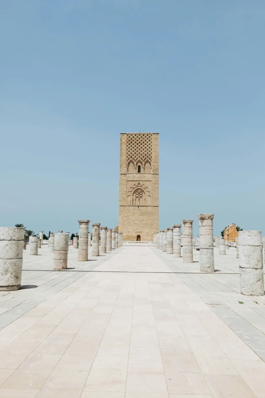 a stone walkway with columns and a clock tower in the background, inspired by Alberto Morrocco, trending on unsplash, les nabis, morocco, blue sky, square, two giant towers
