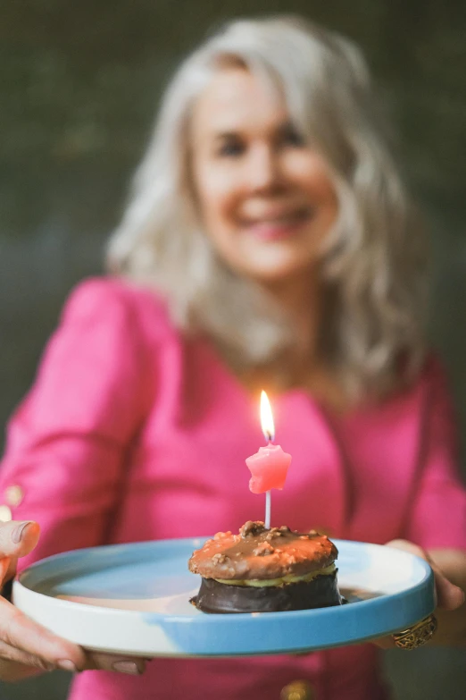 a woman holding a plate with a cupcake on it, a portrait, by Pamela Drew, pexels, happy birthday candles, aging, wholesome, majestic light