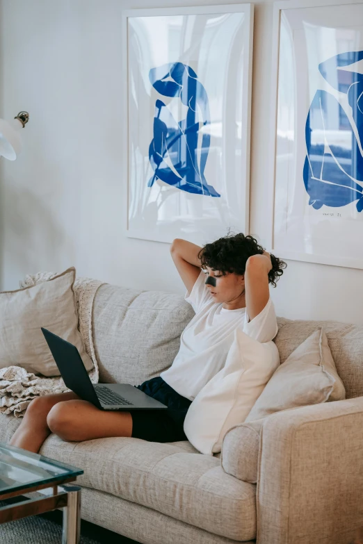a woman sitting on a couch using a laptop, by Nicolette Macnamara, pexels contest winner, happening, dressed in a white t shirt, chill, curly haired, topknot