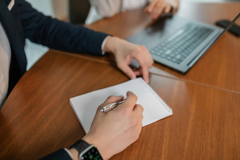 a person sitting at a table with a laptop and a pen