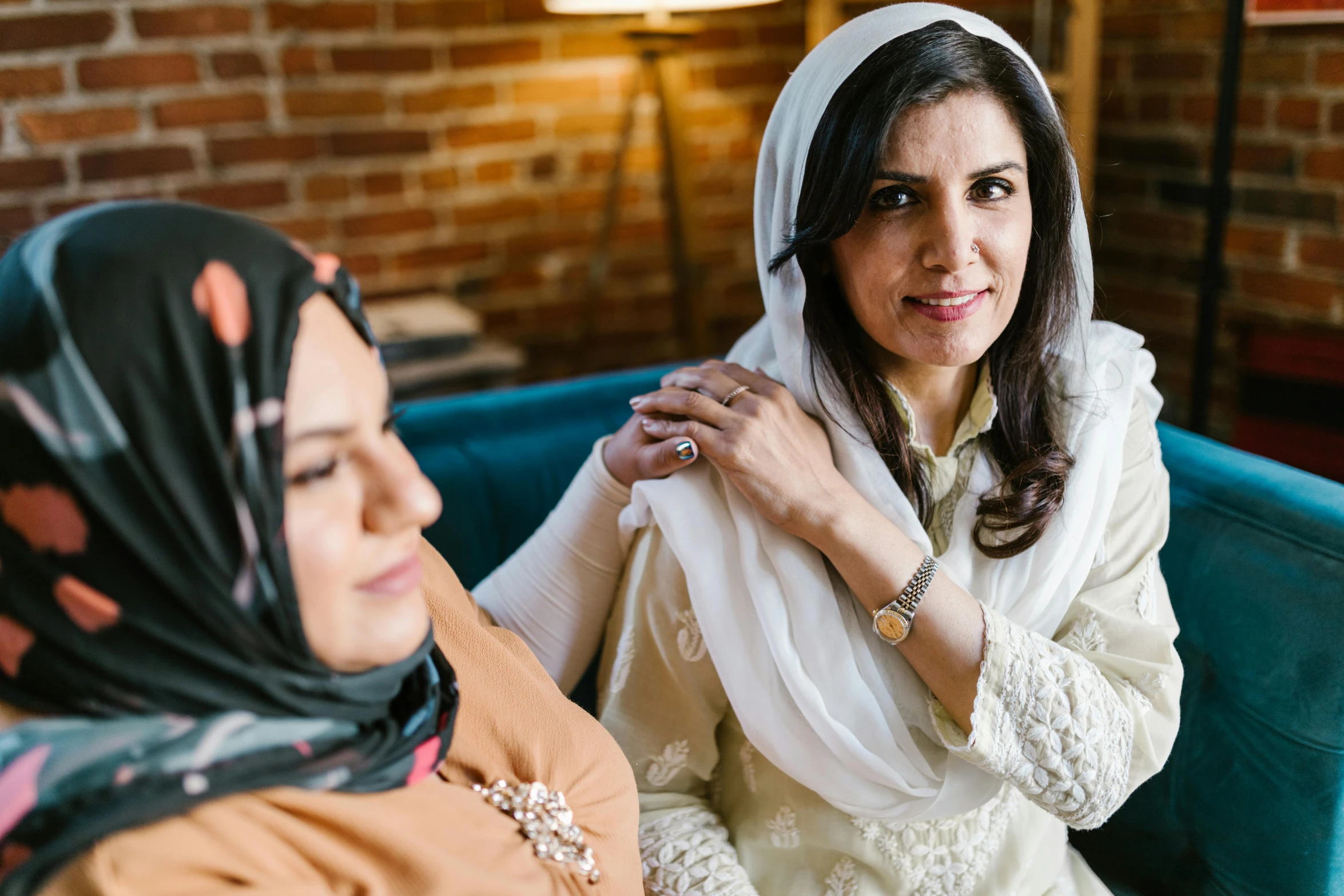 two women sitting next to each other on a couch, a portrait, inspired by Maryam Hashemi, pexels, hurufiyya, looking from shoulder, head scarf, professional image, comforting and familiar