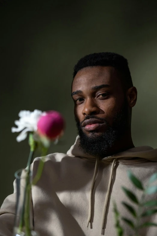 a man with a beard sitting in front of a vase of flowers, jaylen brown, photo of a rose, dark. no text, press photos