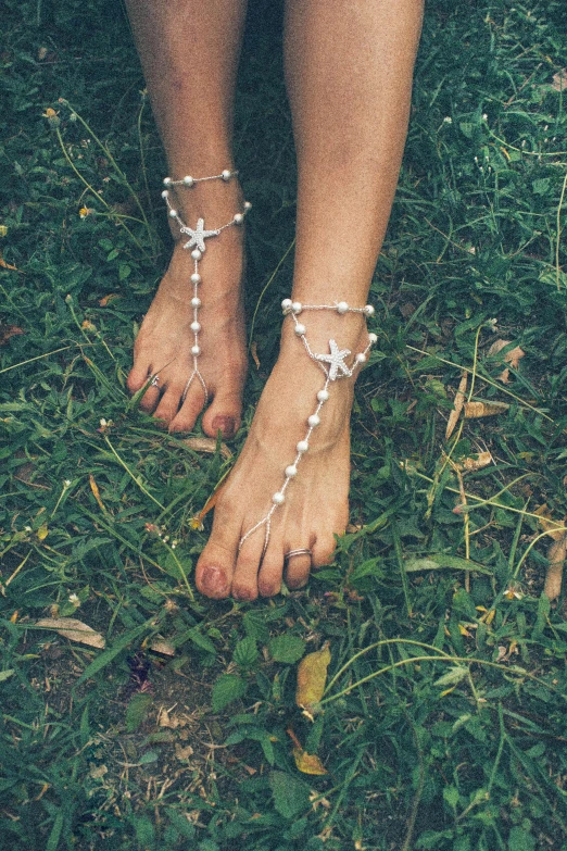 a woman standing on top of a lush green field, an album cover, inspired by Elsa Bleda, unsplash, renaissance, exposed toes, with big starfish, jewelry pearls, white and silver