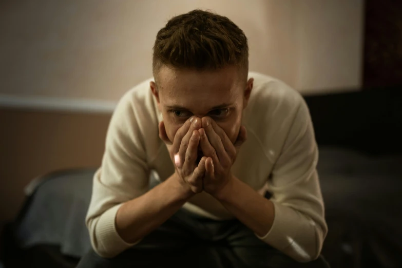 a man sitting on a couch covering his face with his hands, pexels, hyperrealism, pouty, low lights, teenage boy, praying