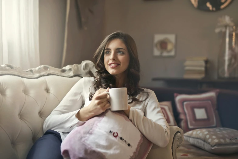 a woman sitting on a couch holding a cup of coffee, by Lucia Peka, pexels, throw pillows, pink, open plan, portrait mode photo