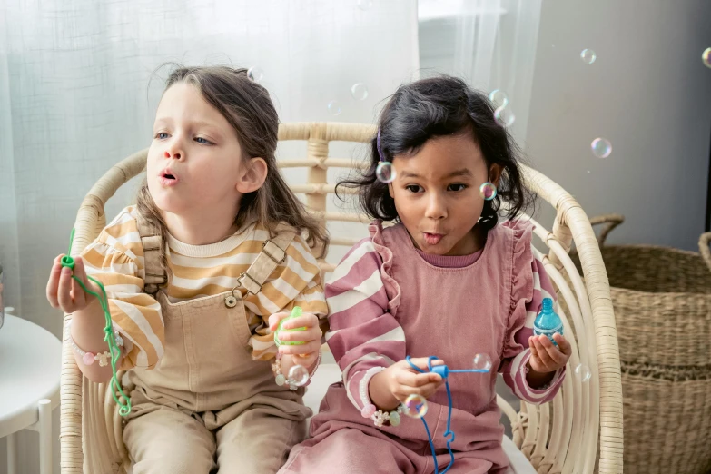 two little girls sitting in a wicker chair blowing bubbles, pexels, happening, earbuds jewelry, two buddies sitting in a room, wrapped in wires and piones, mixed race