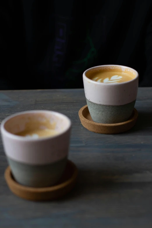 two cups of coffee sitting on top of a wooden table, by Jessie Algie, with celadon glaze, uncropped, slate, vanilla