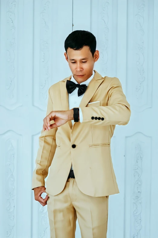 a man wearing a tan suit and a black bow tie, by Basuki Abdullah, gold and white, morning time, cotton, holding gold watch