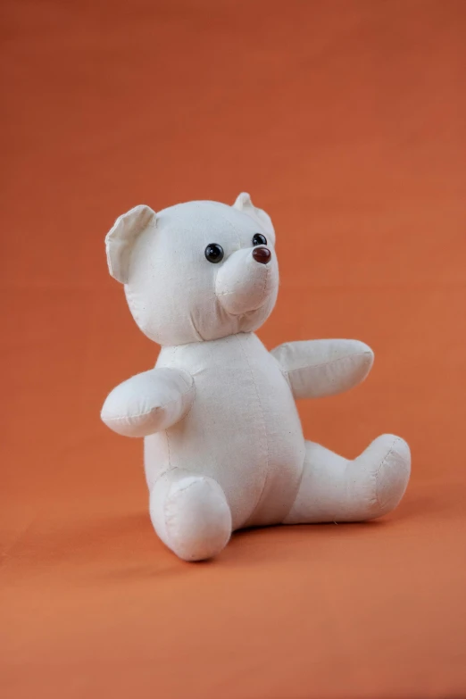 a white teddy bear sitting on an orange surface, on a white table