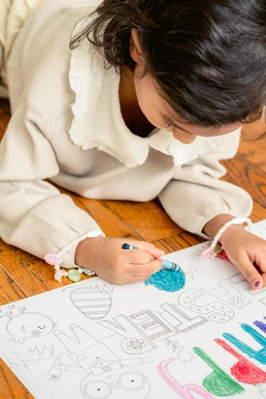 a little girl laying on the floor drawing on a piece of paper, pexels contest winner, process art, puffy sticker, coloring book page, crisp colors, painted overalls