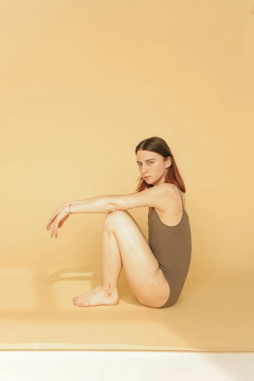 a woman sitting on the ground in a bathing suit, an album cover, by Gavin Hamilton, trending on pexels, realism, muted arm colors, maisie williams, battle pose, synthetic bio skin