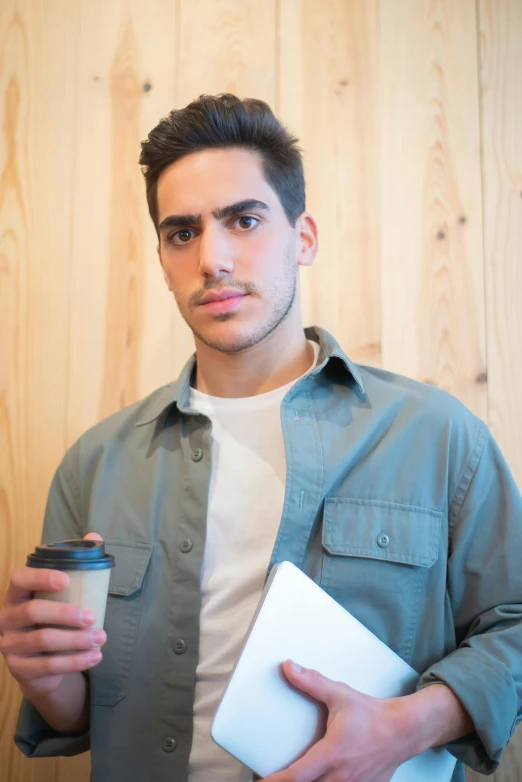 a man holding a cup of coffee and a book, an album cover, inspired by david rubín, trending on unsplash, harsh good looking face, holding a clipboard, young spanish man, non binary model