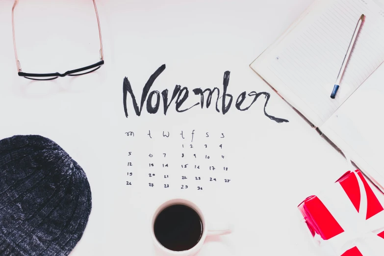 a cup of coffee sitting on top of a desk, by Carey Morris, trending on unsplash, happening, female calendar, november, “modern calligraphy art, background image