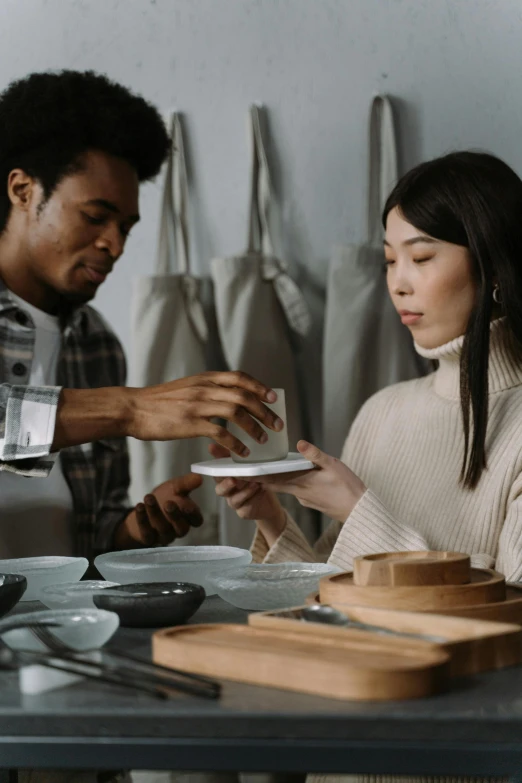 a couple of people that are sitting at a table, inspired by Kanō Naizen, trending on unsplash, renaissance, carrying a tray, ceramic, mixed race, in a workshop