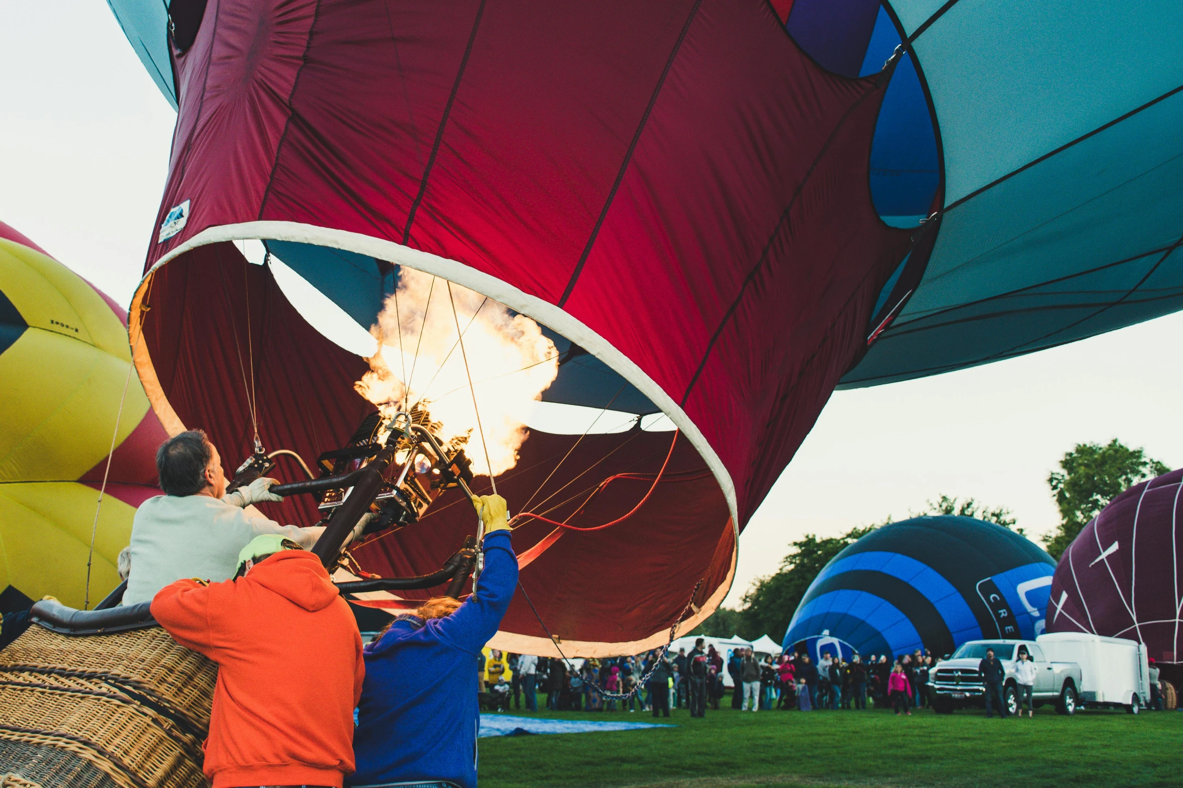 a group of people standing around a hot air balloon, air and fire, event photography, sky blue, helmet is off