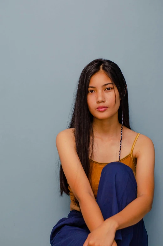 a woman sitting on the floor with her legs crossed, inspired by helen huang, unsplash, minimalism, long thin black hair, blue backdrop, portrait of a japanese teen, wearing a camisole